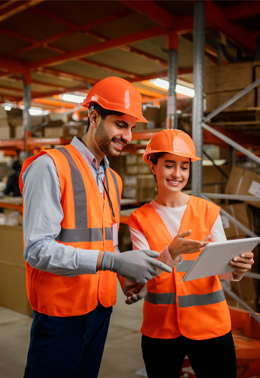 Warehouse workers wearing safety equipment reviewing a plan on a tablet, showcasing collaboration and efficiency in an industrial setting.